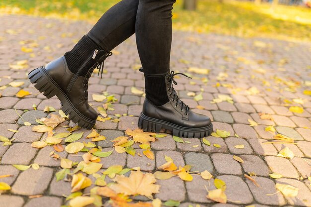 Una mujer con botas negras se encuentra en un camino de ladrillos en hojas de otoño.