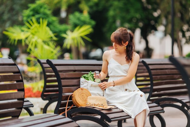 Mujer con botella de agua reutilizable y bolso de bambú, bolsa de algodón con verduras en el parque. Concepto de vacaciones de verano