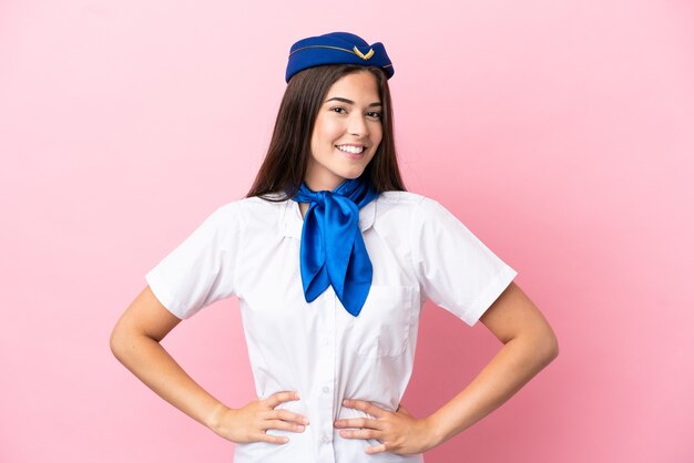 Foto mujer brasileña azafata de avión aislada sobre fondo rosa posando con los brazos en la cadera y sonriendo