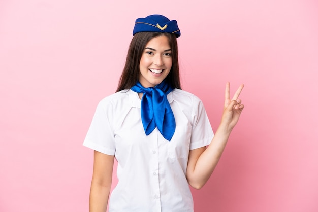 Mujer brasileña azafata de avión aislada sobre fondo rosa sonriendo y mostrando el signo de la victoria