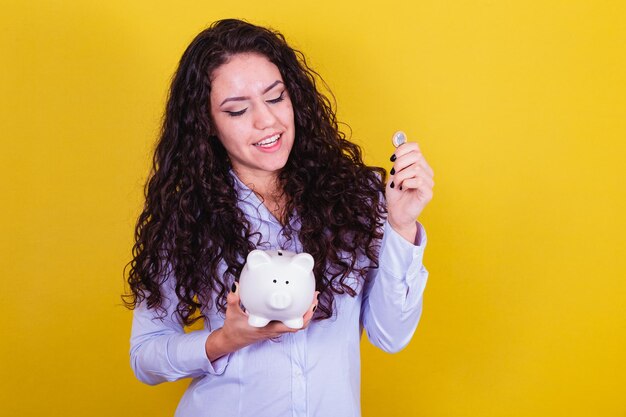 Mujer brasileña caucásica sosteniendo moneda y alcancía concepto de economía financiera ahorro