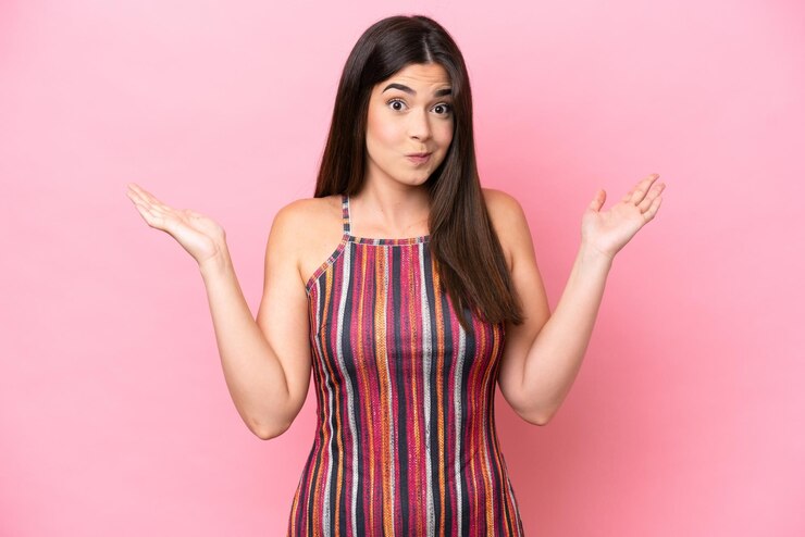 Foto mujer brasileña joven aislada en fondo rosa con dudas mientras levanta las manos