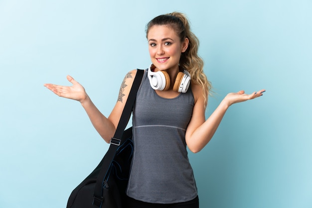 Mujer brasileña joven deporte con bolsa de deporte aislada en azul con expresión facial sorprendida