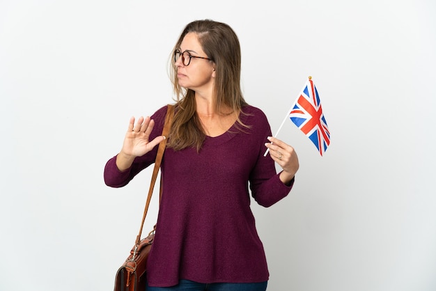 Mujer brasileña de mediana edad sosteniendo una bandera del Reino Unido aislada en la pared blanca haciendo gesto de parada y decepcionado