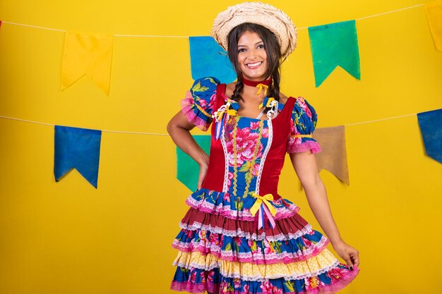 Foto mujer brasileña con ropa de festa de sao joao festa junina sobre fondo amarillo con banderas