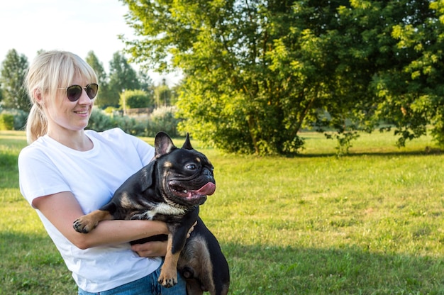 Mujer en brazos con bulldog francés en el parque de verano