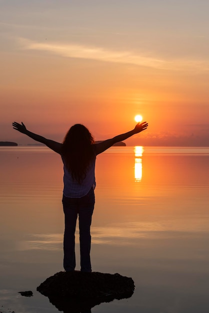 una mujer con los brazos extendidos frente a una puesta de sol