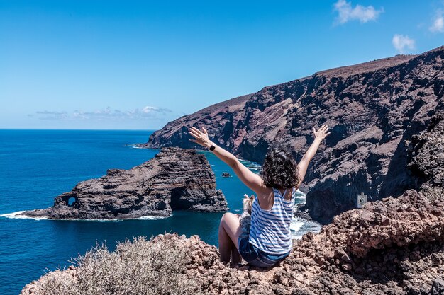 Mujer con los brazos levantados disfrutando de las hermosas vistas de la playa Roque de Santo Domingo en La Palma, Islas Canarias