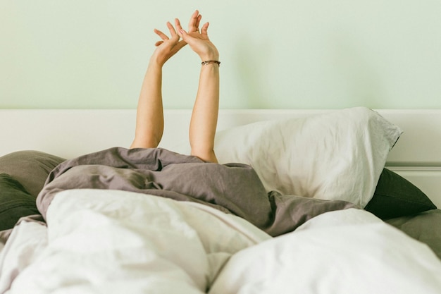 Mujer con los brazos levantados mientras se relaja en la cama en casa