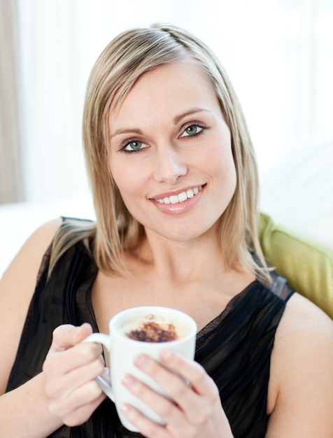 Mujer brillante bebiendo un café sentado en un sofá