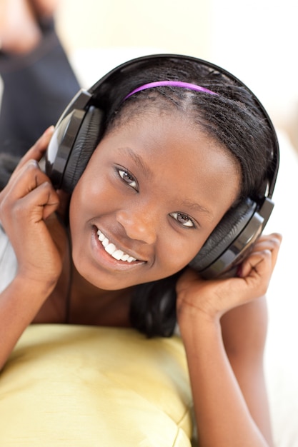 Mujer brillante escuchando música con auriculares acostado en un sofá