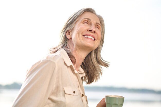 Mujer brillante con taza mirando hacia arriba al aire libre