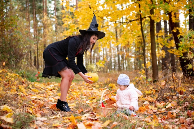 Mujer bruja negra con conejito de niño pequeño en el bosque de otoño fiesta de disfraces de celebración de halloween