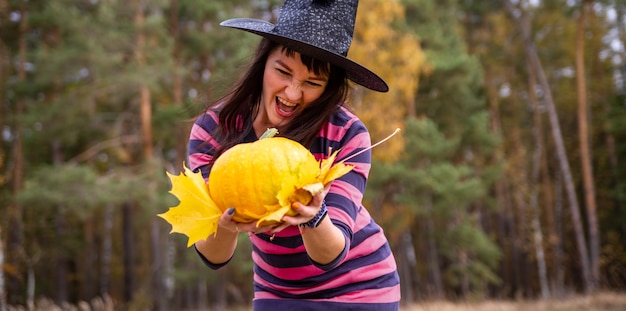 Mujer bruja sosteniendo calabaza con emociones aterradoras en el bosque de otoño