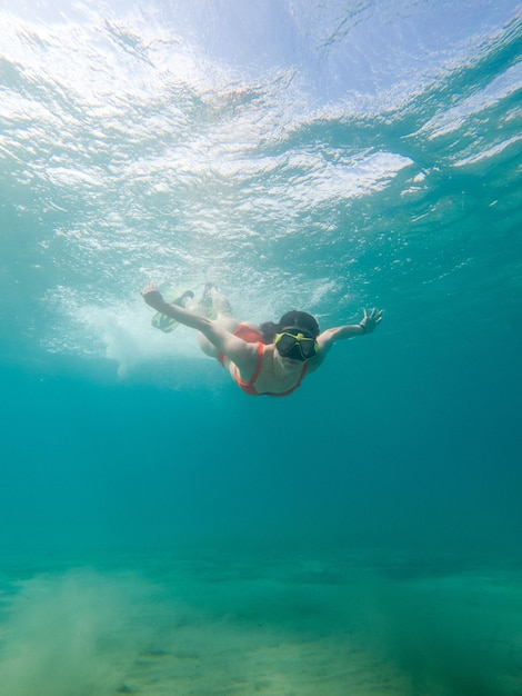 Mujer buceando bajo el agua con máscara de buceo y aletas