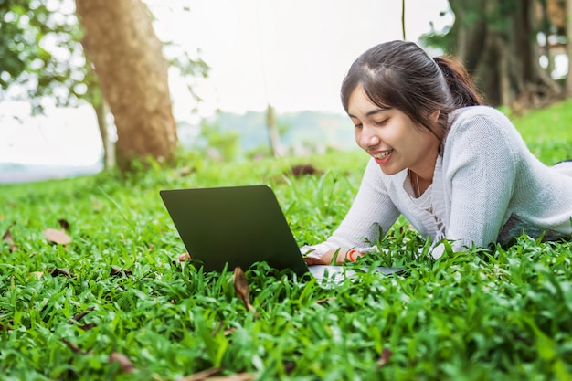 Mujer de Bueatiful con la computadora portátil en hierba verde en parque