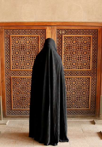 Mujer con burka de pie contra la puerta