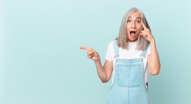 Mujer de cabello blanco de mediana edad que parece sorprendida, dándose cuenta de un nuevo pensamiento, idea o concepto y apuntando hacia un lado