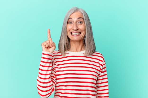 Mujer de cabello blanco de mediana edad que se siente como un genio feliz y emocionado después de darse cuenta de una idea