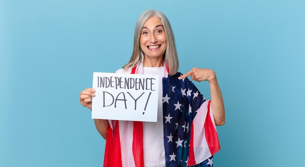 Mujer de cabello blanco de mediana edad que se siente feliz y apunta a sí misma con un entusiasmo. concepto del día de la independencia