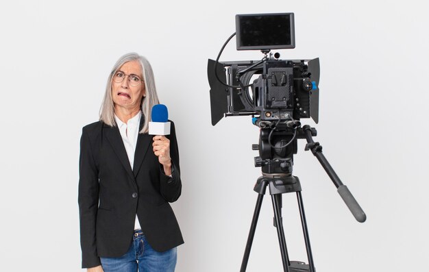 Foto mujer de cabello blanco de mediana edad que se siente perpleja y confundida y que sostiene un micrófono. concepto de presentador de televisión