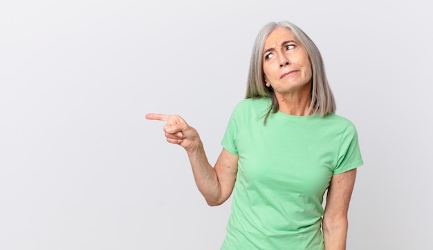 Mujer de cabello blanco de mediana edad que se siente triste, molesta o enojada y mira hacia un lado y apunta hacia el lado