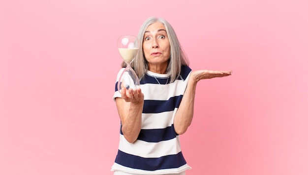 mujer de cabello blanco de mediana edad sosteniendo un reloj de arena