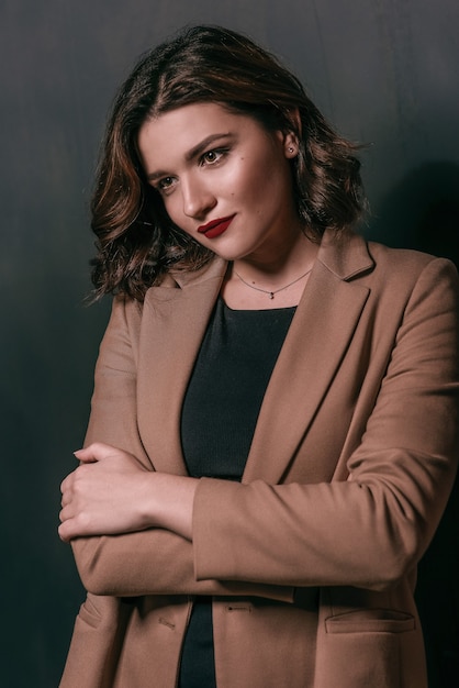 Mujer con cabello castaño corto con elegante maquillaje en vestido negro y chaqueta beige