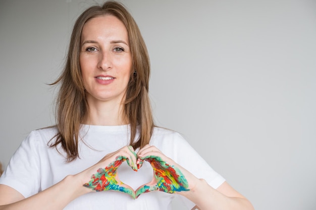 Mujer de cabello castaño muestra corazón con manos pintadas en estudio