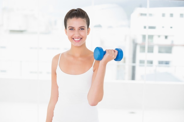 Mujer de cabello castaño natural dinámico en ropa deportiva blanca levantando una pesa