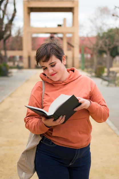 Mujer con cabello corto lee un libro y sonríe en un parque