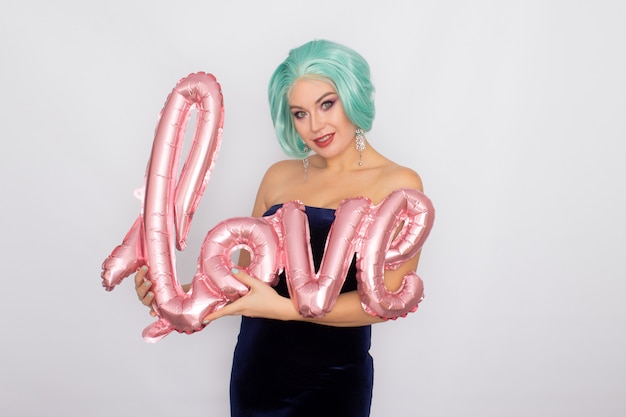 Mujer con cabello corto de menta en vestido de terciopelo azul oscuro con globo con la palabra amor