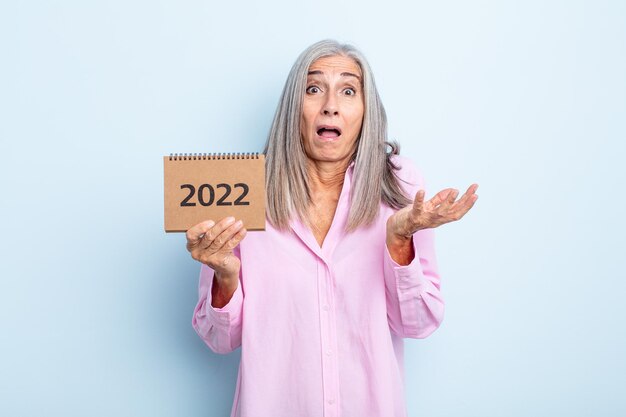 Mujer de cabello gris de mediana edad asombrada y asombrada con un increíble concepto de calendario sorpresa 2022