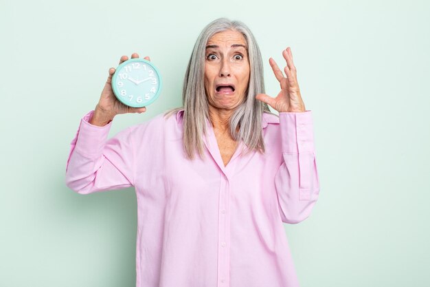 Mujer de cabello gris de mediana edad gritando con las manos en el aire. concepto de despertador