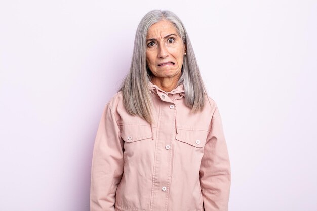 Foto mujer de cabello gris de mediana edad que parece desconcertada y confundida, mordiendo el labio con un gesto nervioso, sin saber la respuesta al problema