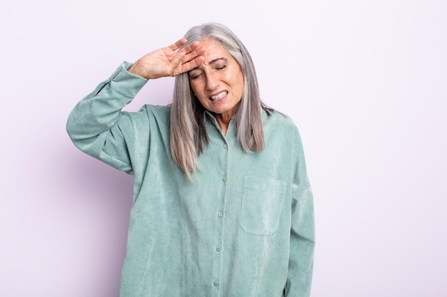 Mujer de cabello gris de mediana edad que parece estresada, cansada y frustrada, secándose el sudor de la frente, sintiéndose desesperanzada y exhausta