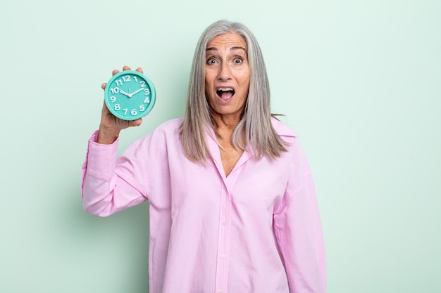 Mujer de cabello gris de mediana edad que parece muy conmocionada o sorprendida. concepto de reloj despertador