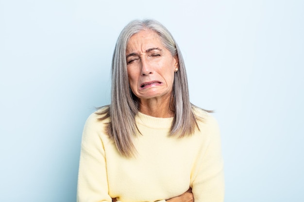 Mujer de cabello gris de mediana edad que se siente ansiosa, enferma, enferma e infeliz, que sufre dolor de estómago o gripe