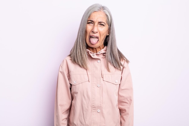 Mujer de cabello gris de mediana edad que se siente disgustada e irritada, que saca la lengua, que no le gusta algo desagradable y asqueroso