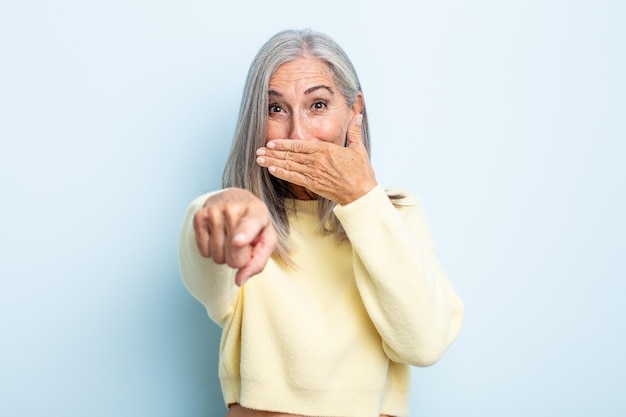 Mujer de cabello gris de mediana edad riéndose de ti, señalando a la cámara y burlándose o burlándose de ti