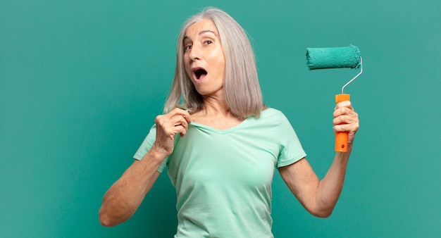 Mujer de cabello gris de mediana edad con un rodillo de pintura decorando su pared