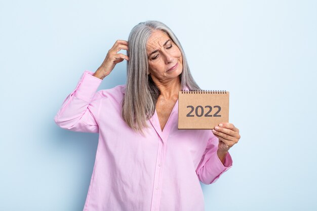 Foto mujer de cabello gris de mediana edad sonriendo felizmente y soñando despierto o dudando. concepto de calendario 2022