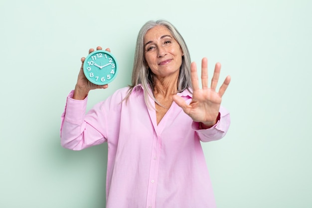 Mujer de cabello gris de mediana edad sonriendo y mirando amigable, mostrando el número cinco. concepto de reloj despertador