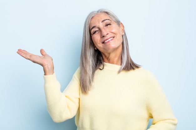 Mujer de cabello gris de mediana edad sonriendo, sintiéndose segura, exitosa y feliz, mostrando concepto o idea en el espacio de la copia en el lateral