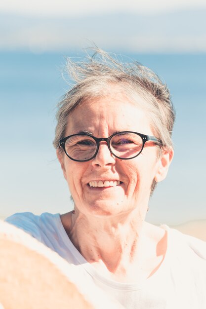 Mujer con cabello gris en la playa durante un día súper soleado concepto de libertad senior copia espacio sol