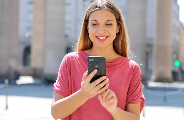 Mujer con cabello largo charlando en el teléfono inteligente en las calles de la ciudad