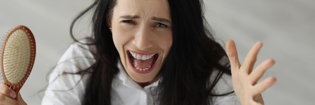 Mujer con cabello largo gritando y sosteniendo un peine en sus manos problemas de pérdida de cabello después de la anterior