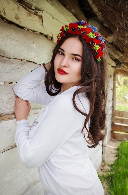 mujer con cabello largo y oscuro en blusa ucraniana y en una corona en una aldea étnica al aire libre en Ucrania