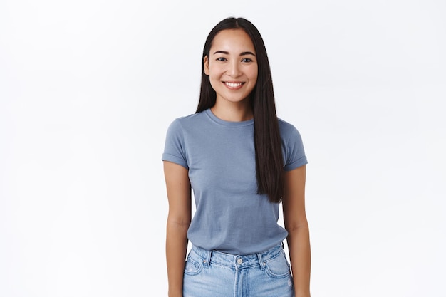 Mujer con cabello largo y oscuro, camiseta y jeans, sonriendo alegremente, pose casual con los brazos hacia abajo, expresando alegría, emociones despreocupadas y relajadas