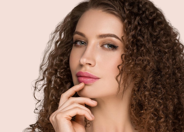 Mujer de cabello largo y rizado morena que toca la belleza de la cara cerca del retrato femenino. Fondo de color rosa